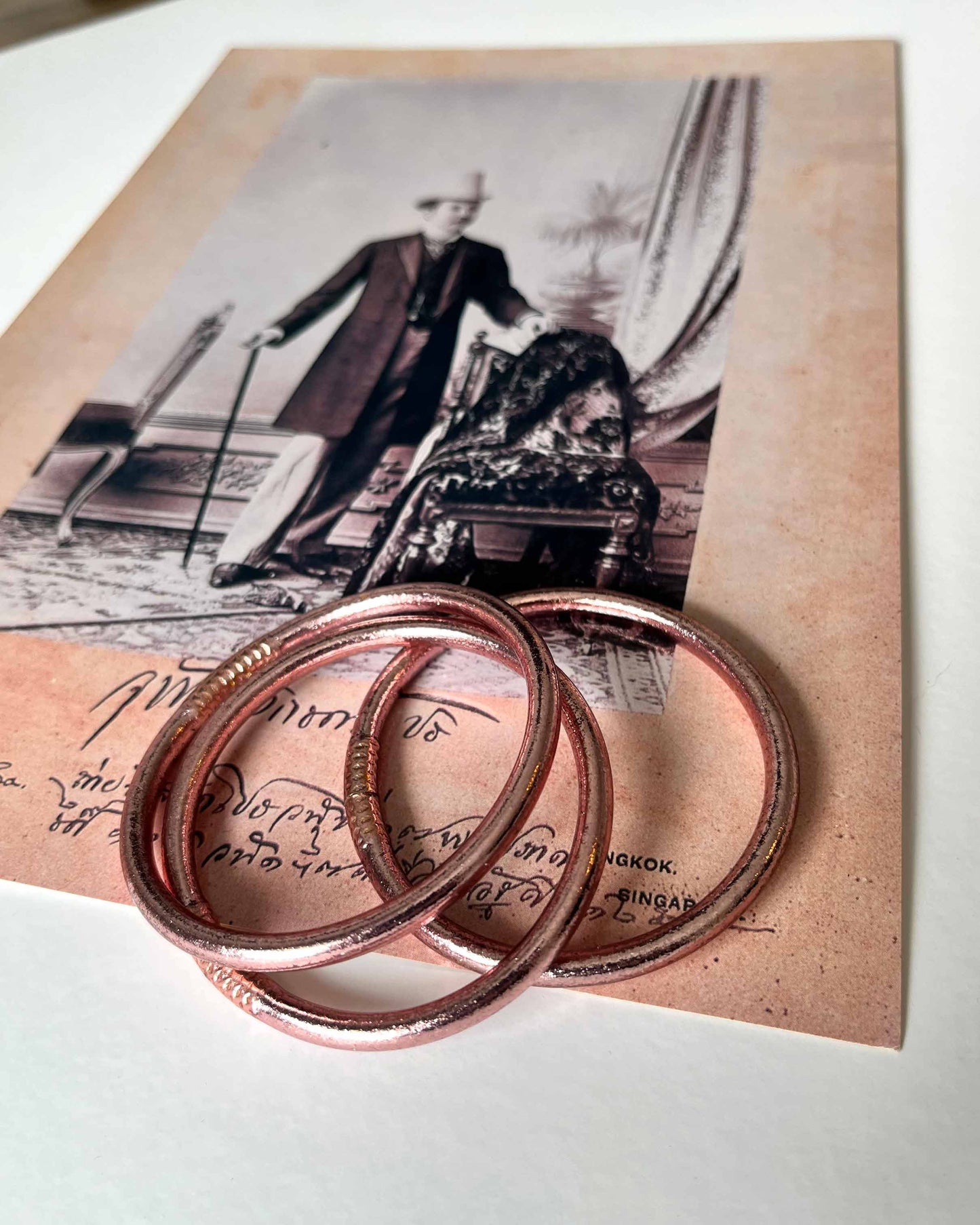 Chunky Kumlai Buddhist bangles in rose gold, placed on a vintage photo.