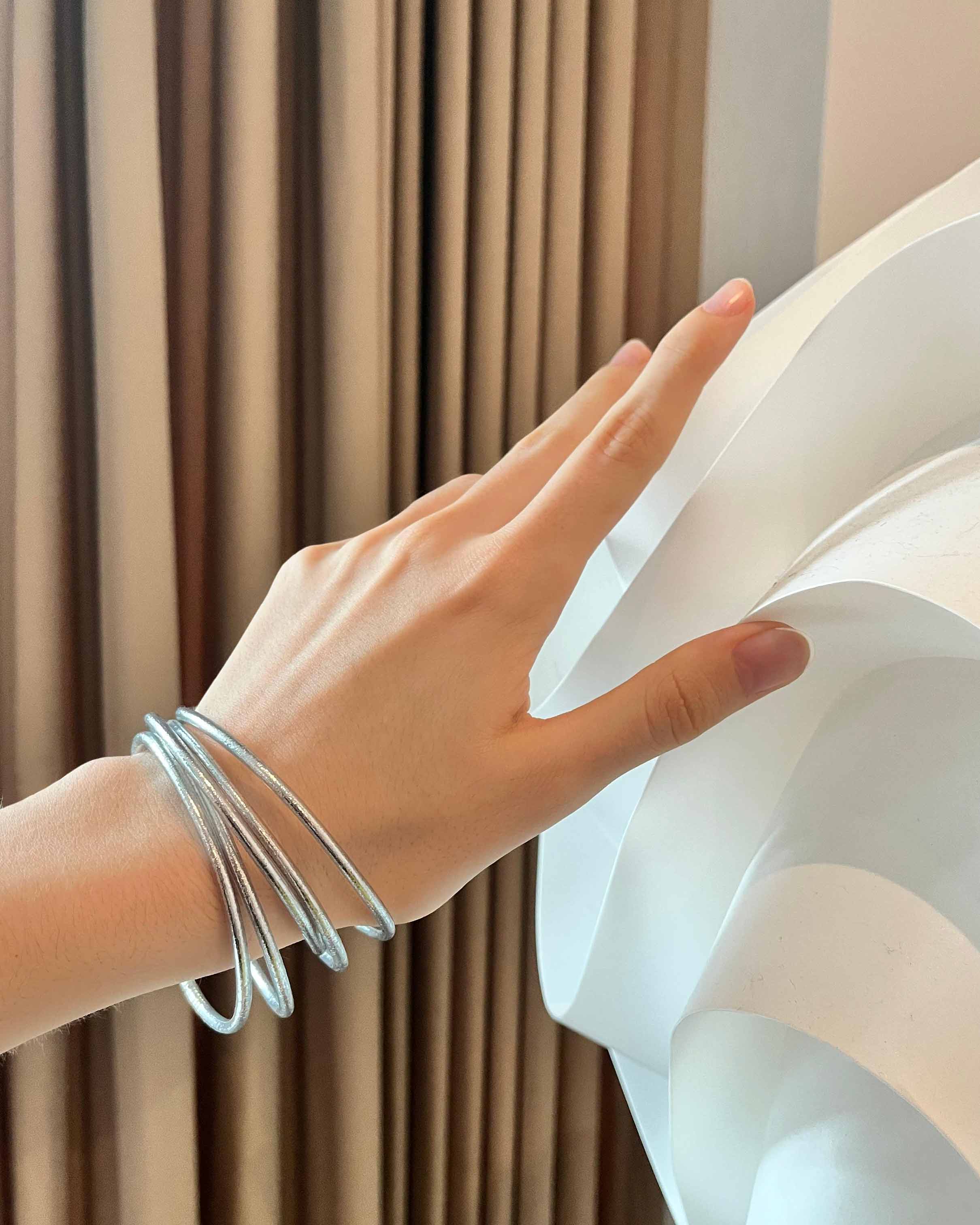 Pulseras budistas Kumlai en plata clásica, estilo fino, usadas junto a una lámpara de diseño.