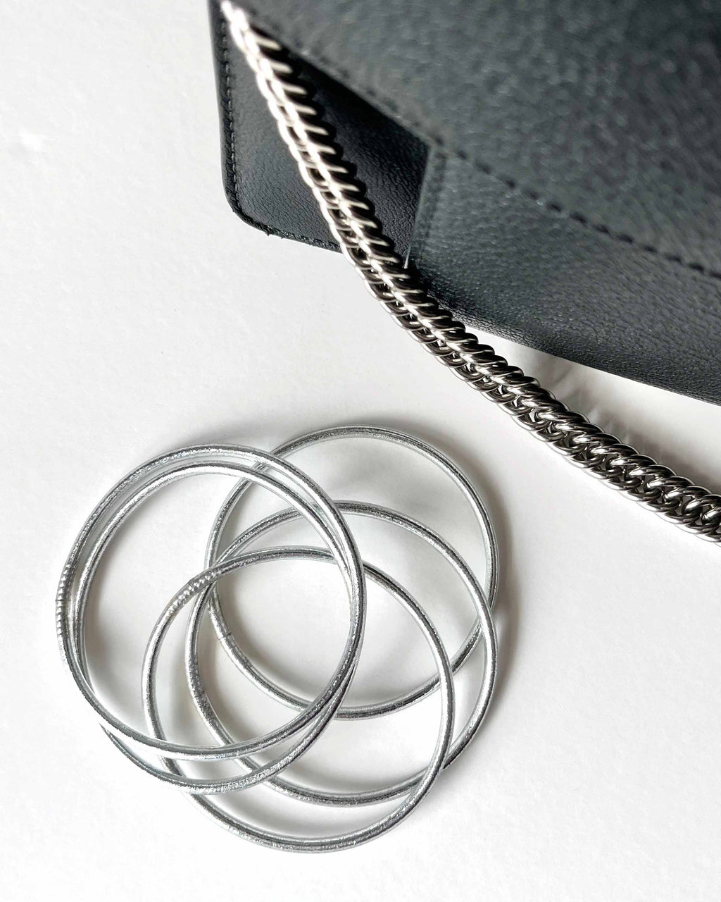Pulseras budistas Kumlai en plata clásica, estilo fino, junto a un bolso de cuero negro.