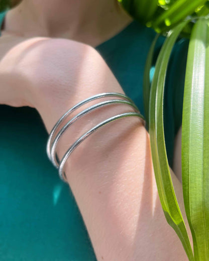 Thin Kumlai Buddhist bangles in Classic Silver worn with a teal top.