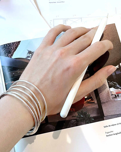 Slim Kumlai Buddhist bangles in classic silver, worn against an architecture magazine background.