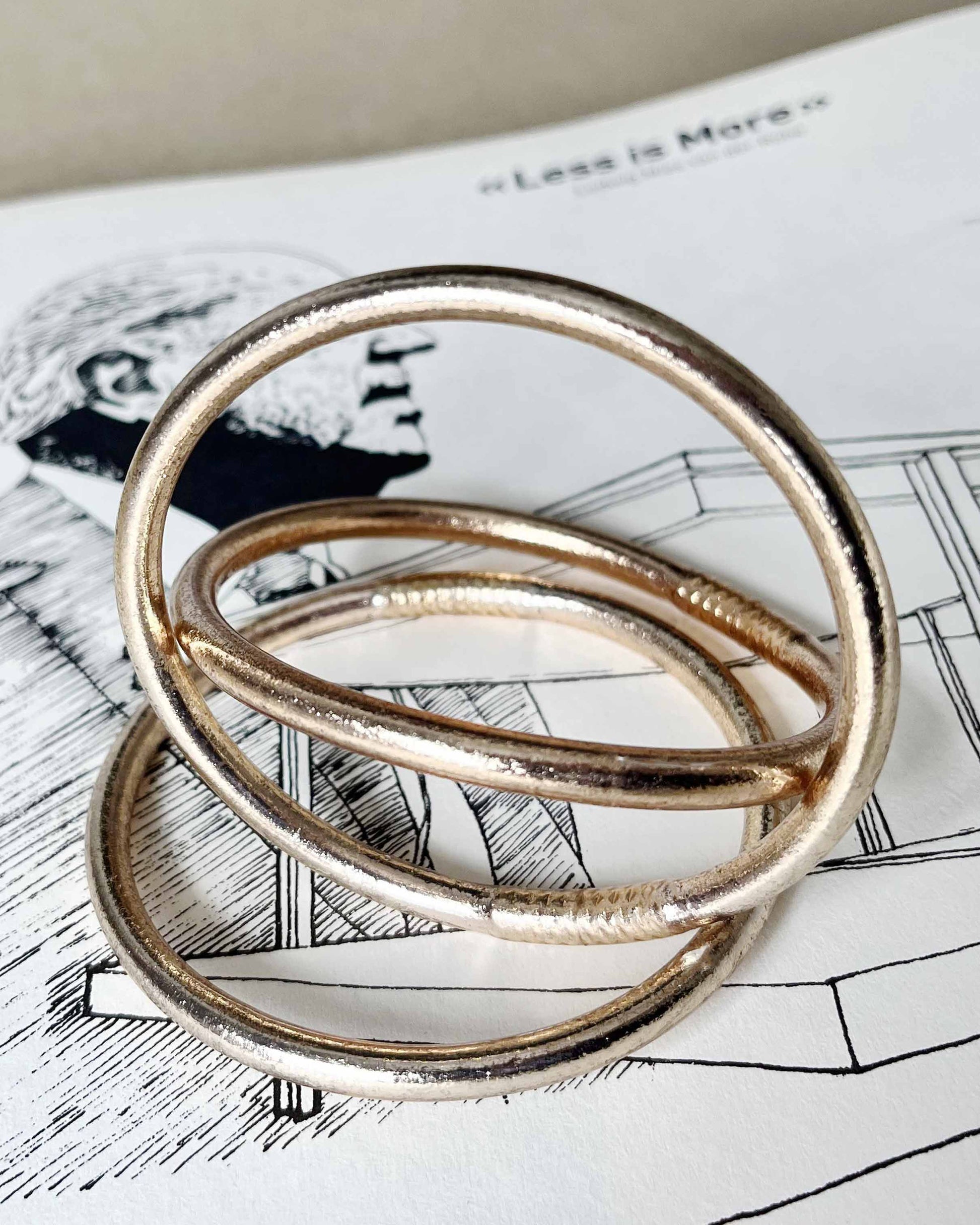 Chunky Kumlai Buddhist bangles in champagne gold, placed on an architecture book.