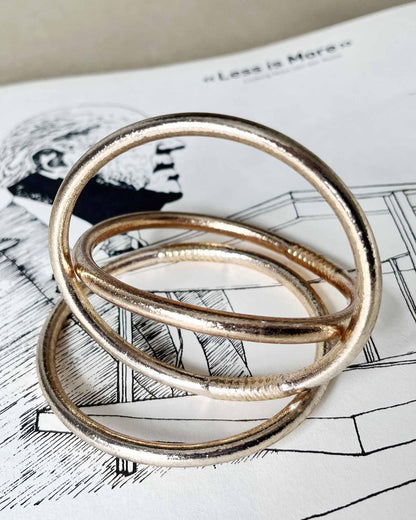 Chunky Kumlai Buddhist bangles in champagne gold, placed on an architecture book.