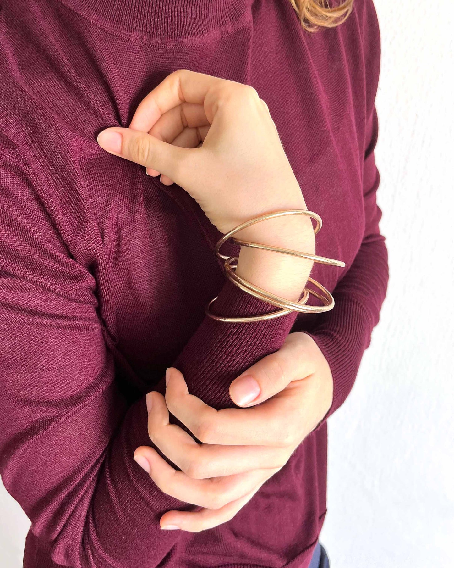 Slim Kumlai Buddhist bangles in champagne gold, worn with a thin burgundy sweater.