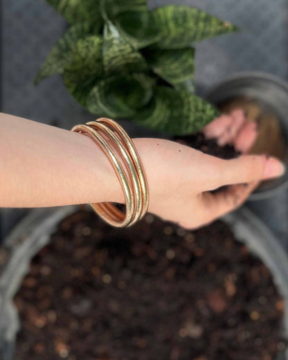 Chunky Kumlai Buddhist bangles in champagne gold, worn while repotting a small plant.