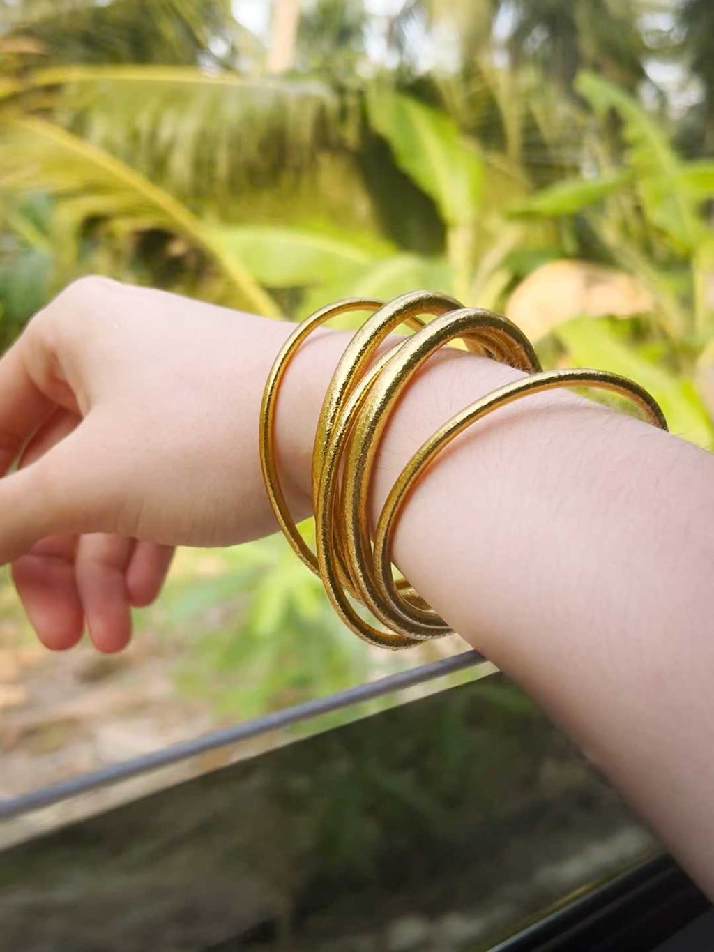 Kumlai Buddhist bangles in classic gold, slim style, seen from a car window.