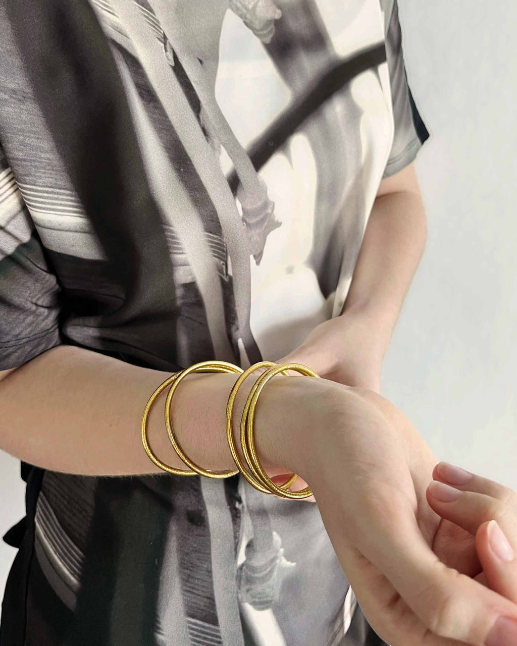 Kumlai Buddhist bangles in classic gold, slim style, worn with a printed top. (2)