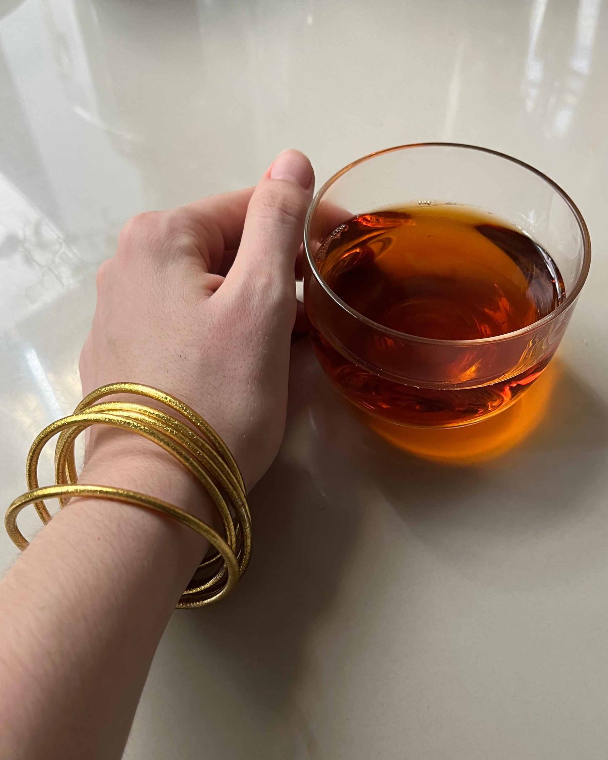 Slim Kumlai Buddhist bangles in classic gold, worn while drinking a cup of tea.