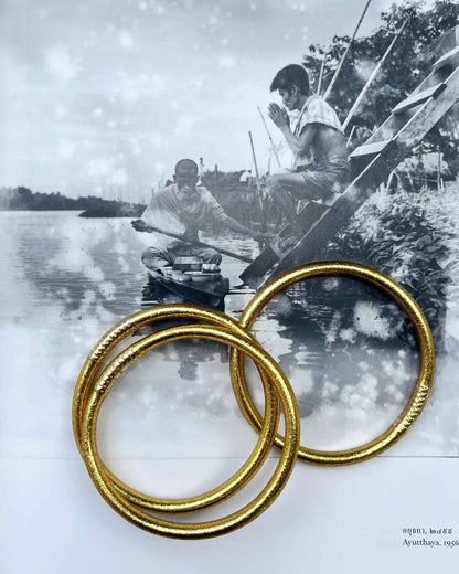 Chunky Kumlai Buddhist bangles in classic gold, placed on a vintage photo book.