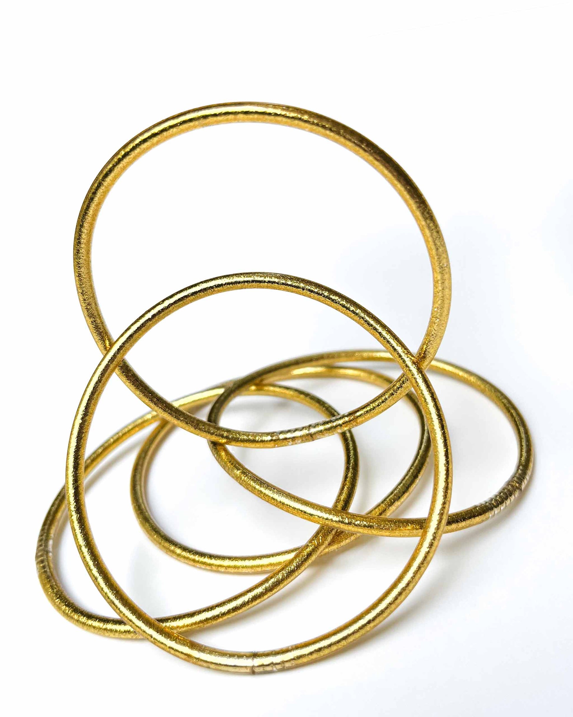 Thin Kumlai Buddhist bangles in Classic Gold on a white background.