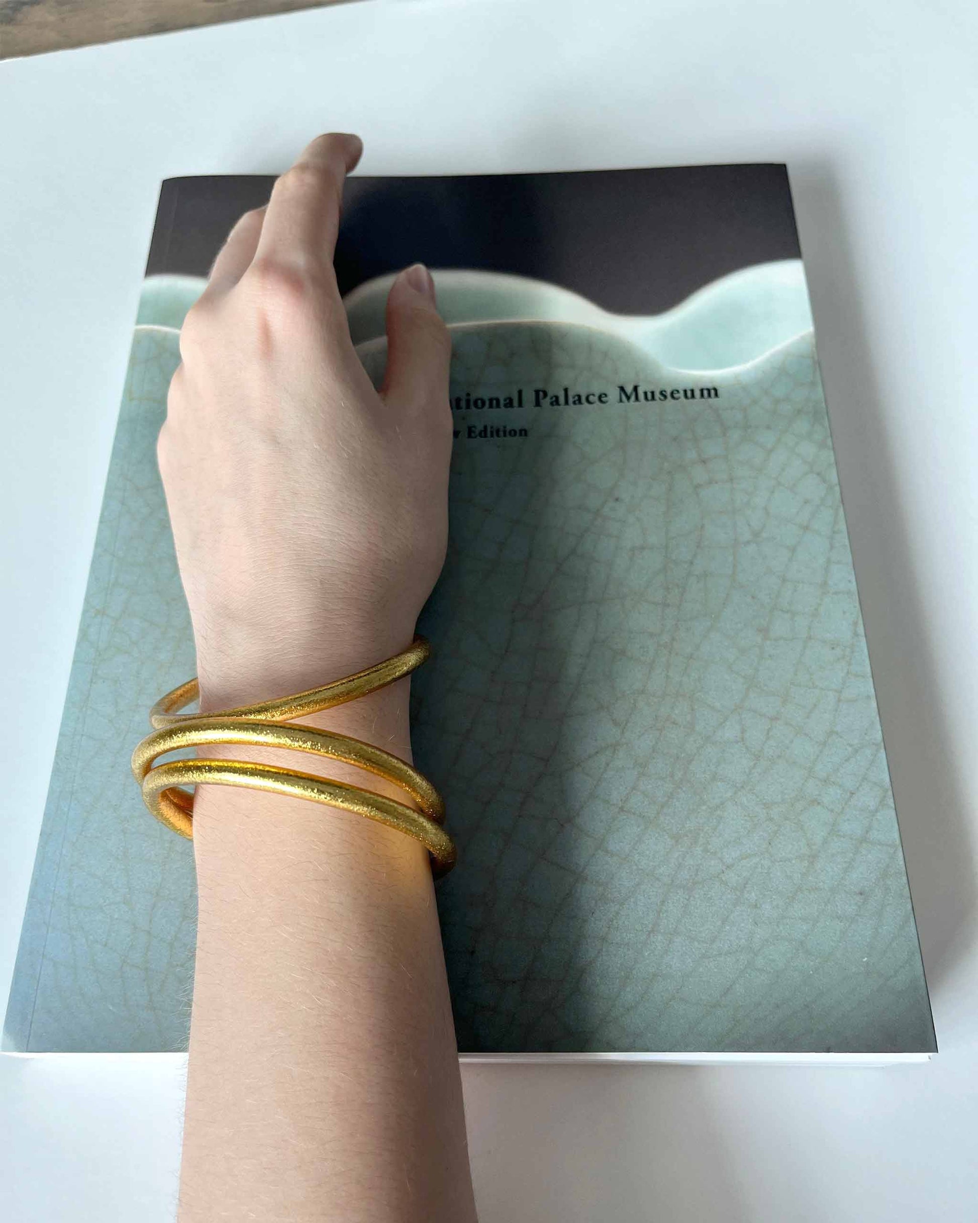 Chunky Kumlai Buddhist bangles in Classic Gold, worn on an art book.