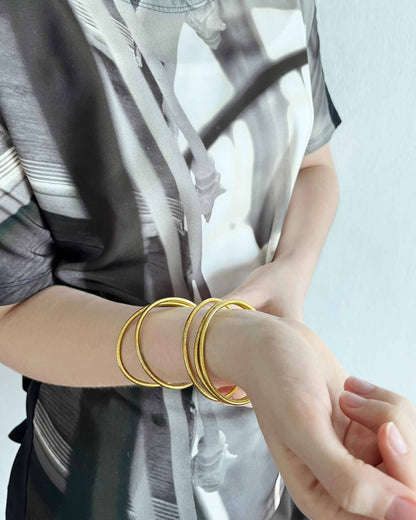 Slim Kumlai Buddhist bangles in classic gold, worn with a Maison Margiela top.