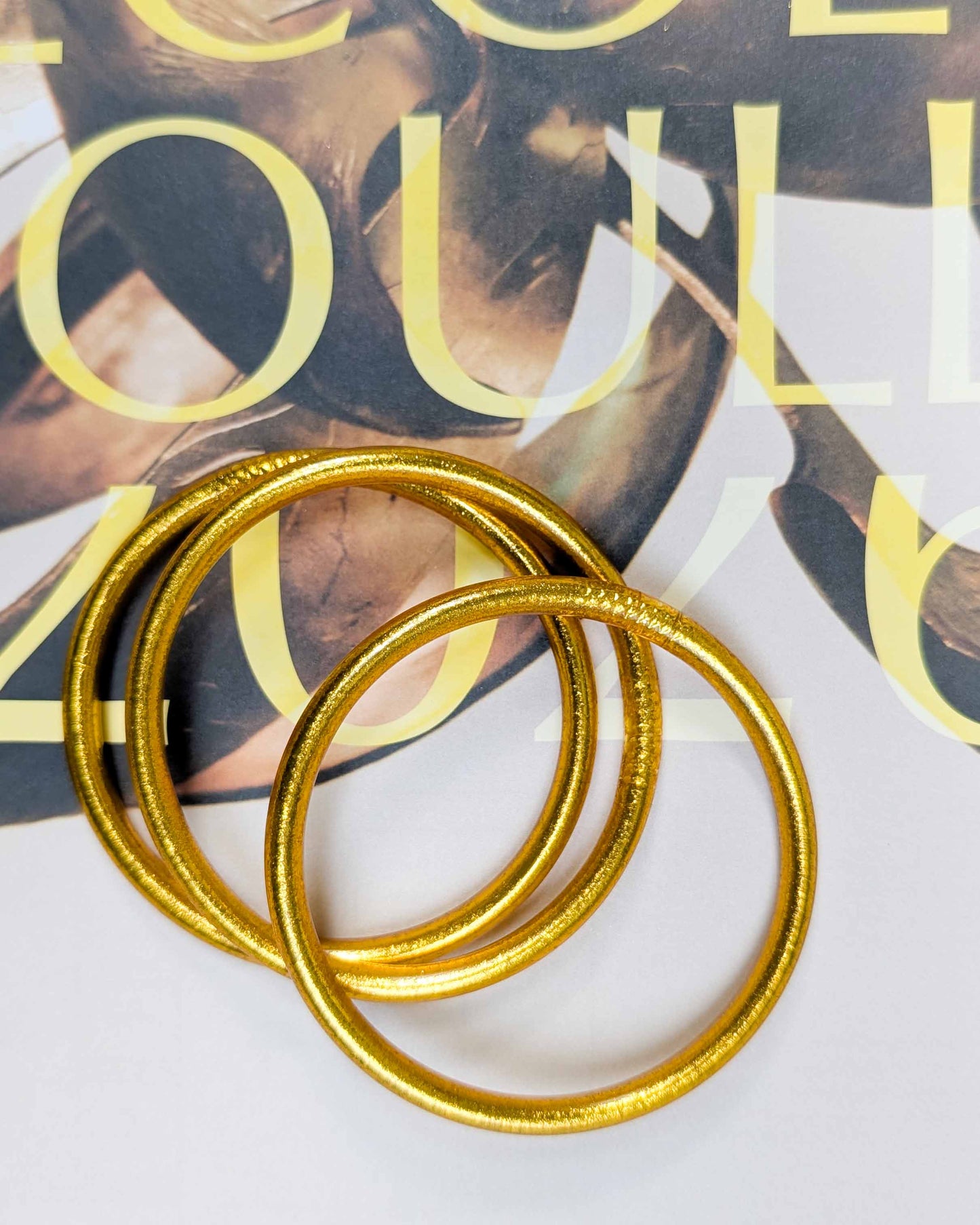 Chunky Kumlai Buddhist bangles in rich gold, placed on a poster.