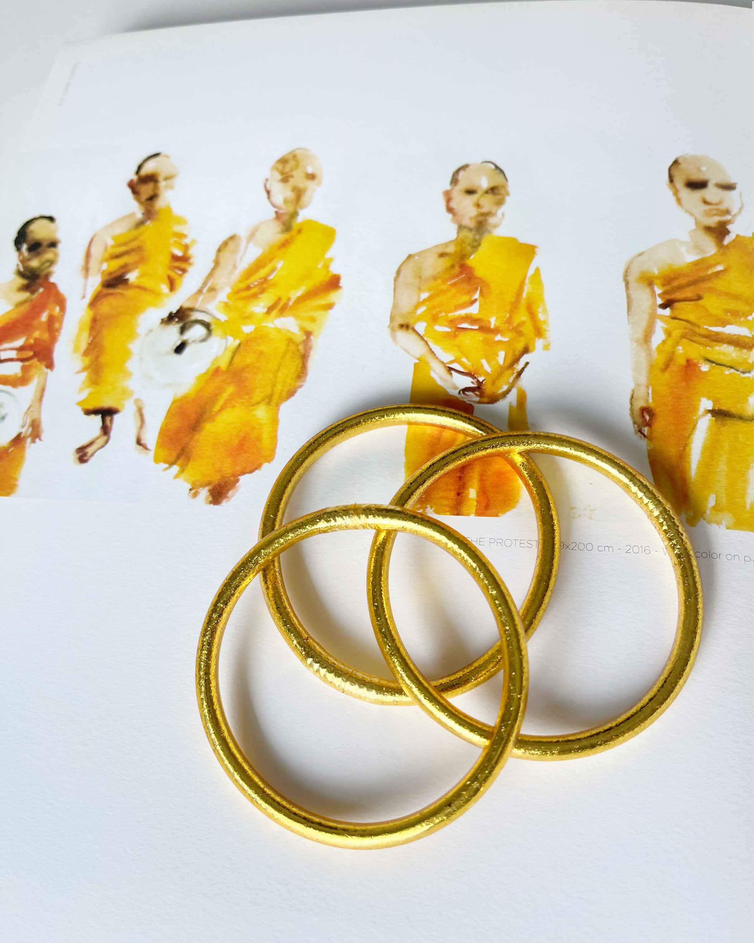 Pulseras budistas Kumlai en oro rico, estilo grueso, colocadas sobre una ilustración.