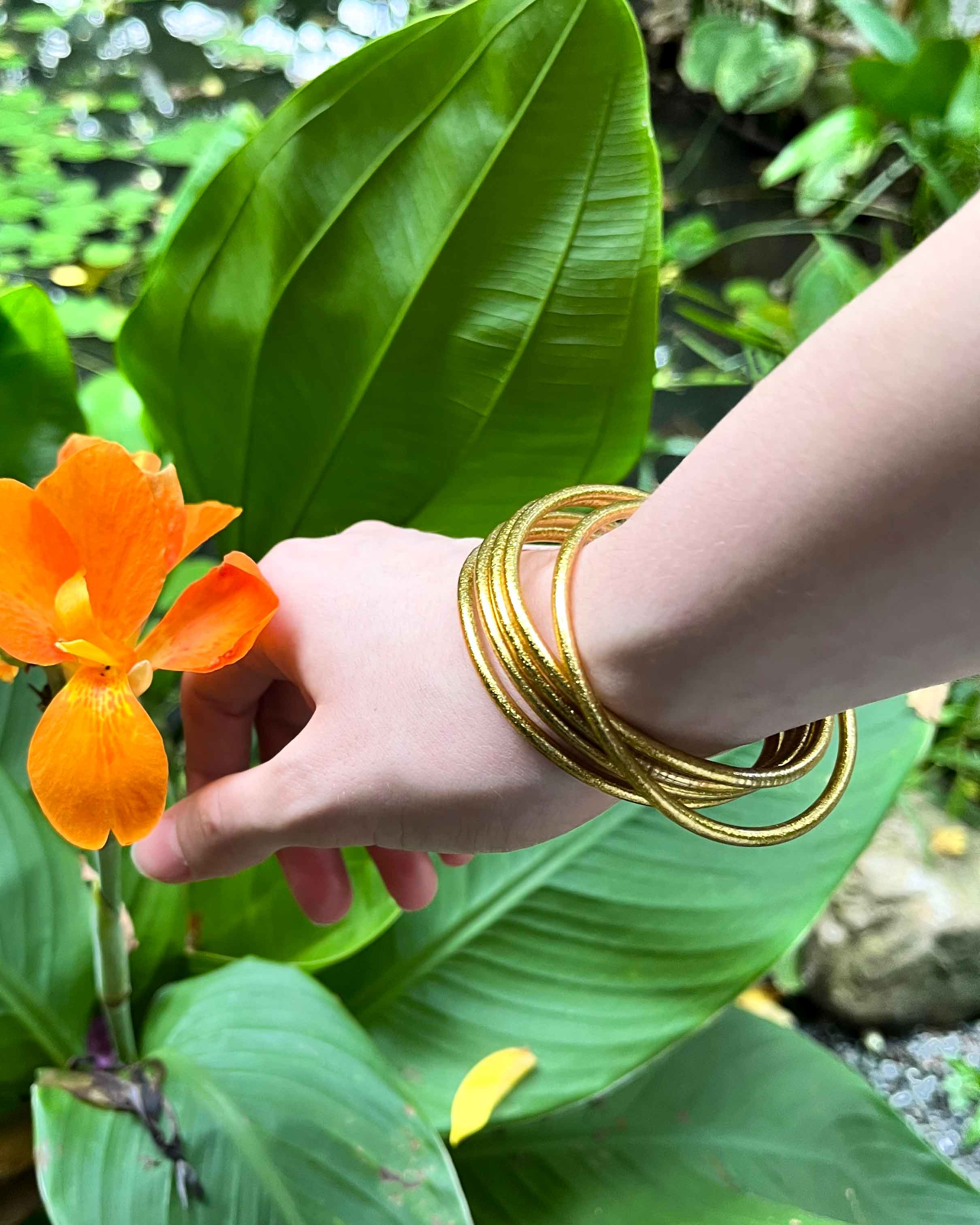 Pulseras budistas Kumlai en oro clásico, estilo fino, sobre hojas y flores naranjas.