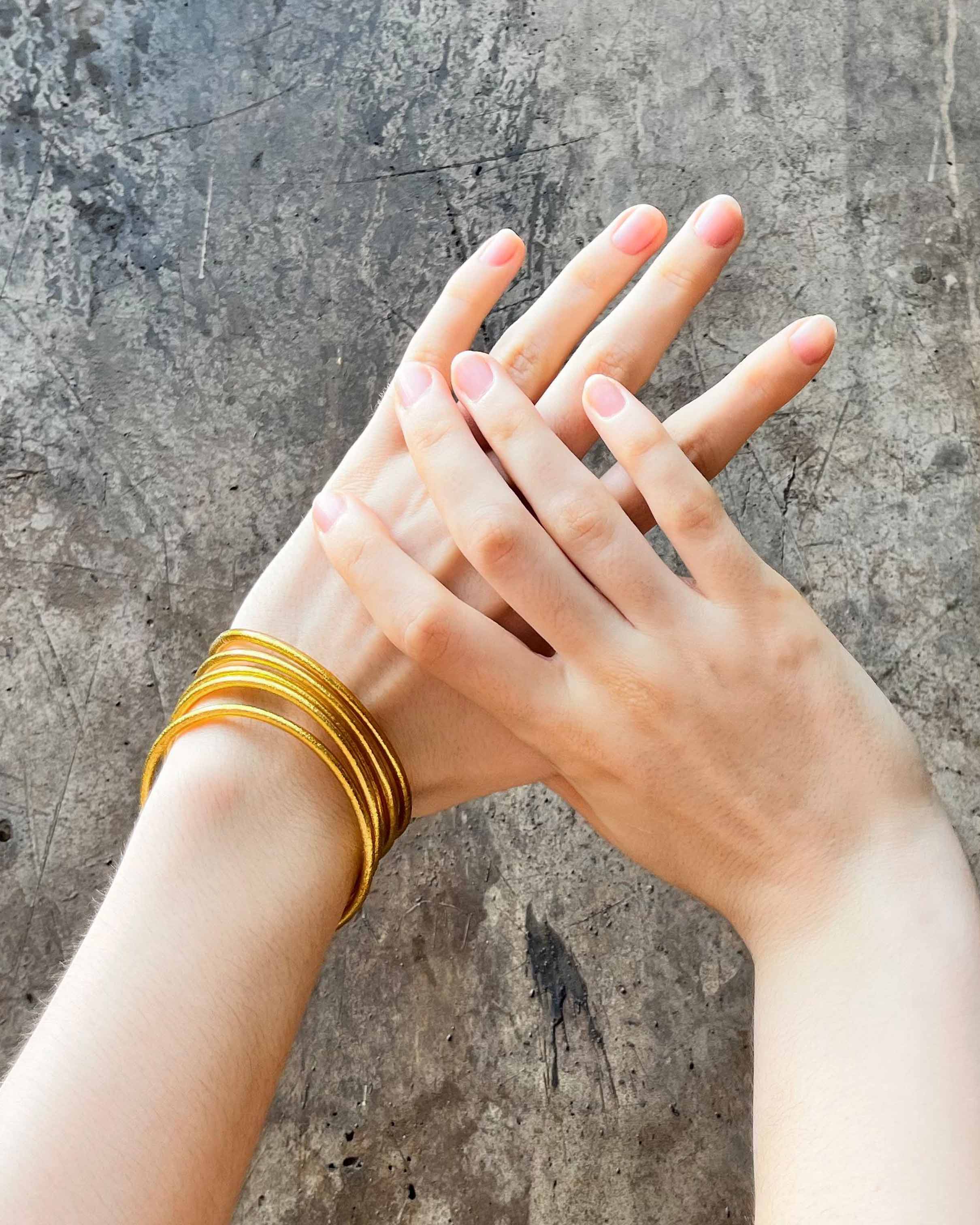 Pulseras budistas Kumlai en oro rico, estilo fino, sobre un muro de concreto envejecido.