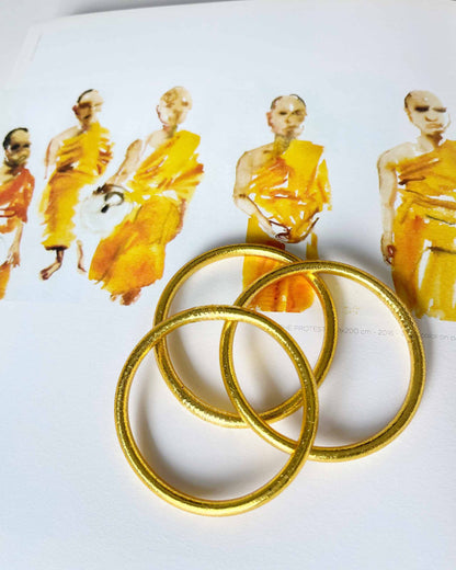 Chunky Kumlai Buddhist bangles in Rich Gold, placed on an illustration.