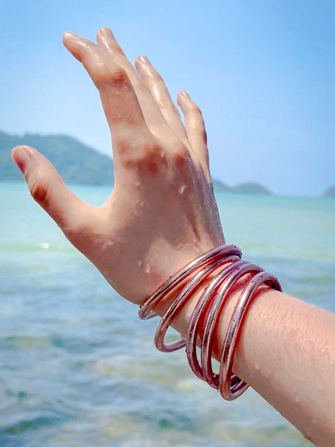 Kumlai Buddhist bangles in rose gold, chunky style, worn at the beach.