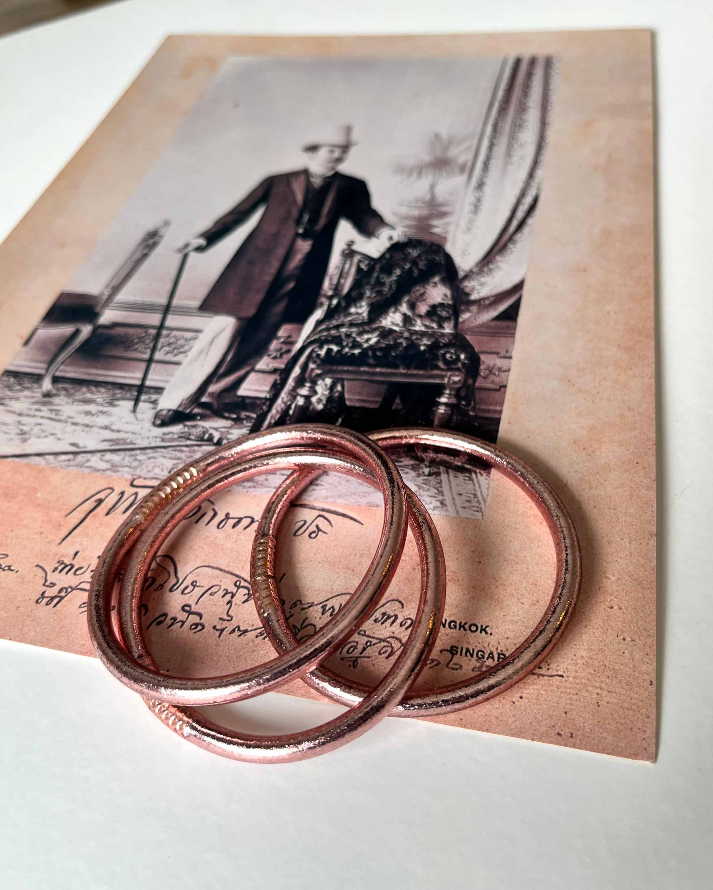 Pulseras budistas Kumlai en oro rosa, estilo grueso, colocadas sobre una foto vintage.