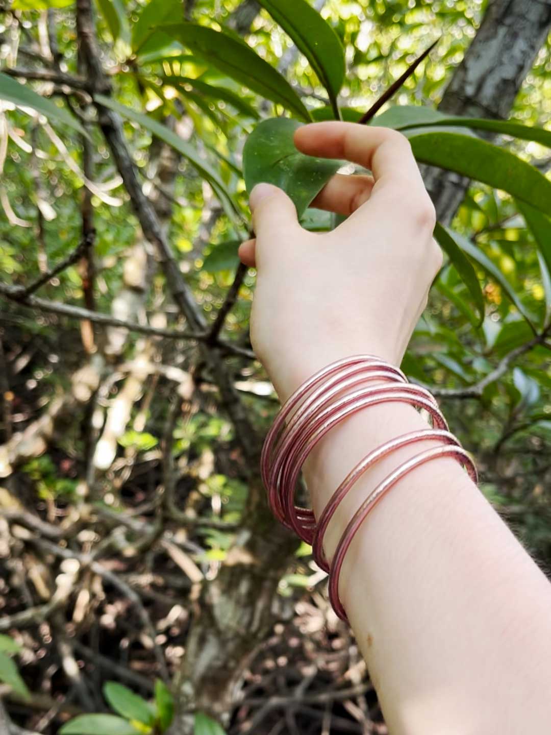 Kumlai Buddhist bangles in rose gold, slim style, worn against a mangrove forest backdrop.