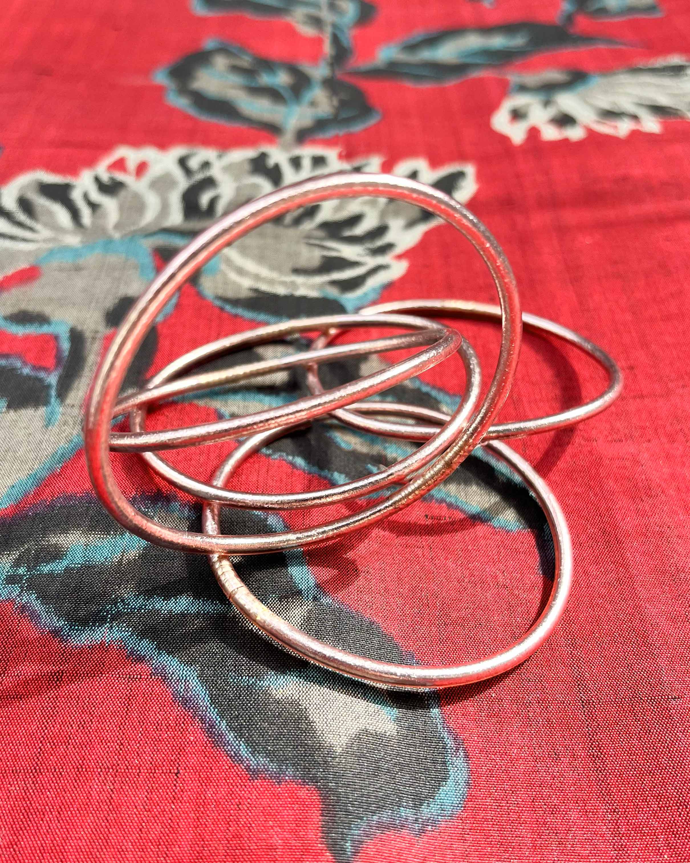 Kumlai Buddhist bangles in rose gold, slim style, placed on silk fabric with floral patterns.