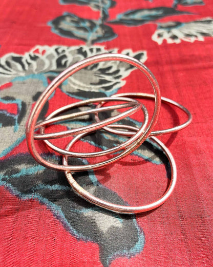 Slim Kumlai Buddhist bangles in rose gold, placed on silk fabric with floral patterns.